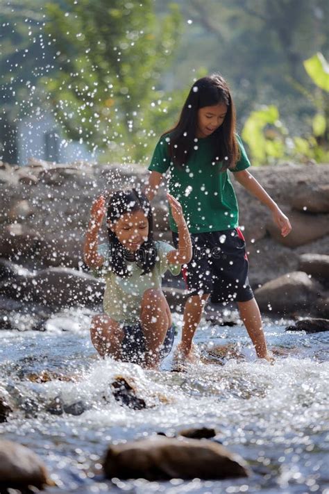 Two Asian Siblings Playing Splash Water On The Waterfall Together With