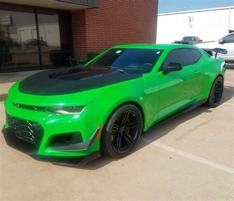 A Green Chevrolet Camaro Is Parked In A Parking Lot Next To A Brick