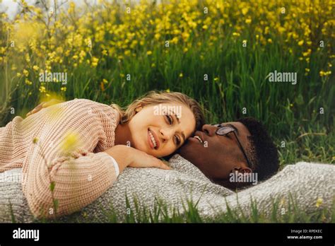 Young Interracial Couple Lying On The Grass In Meadow Relaxed Young