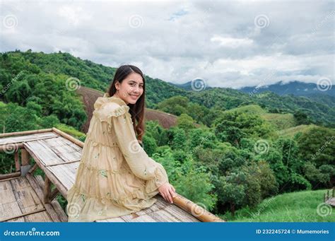 Asian Woman In Yellow Dress Sitting At Wooden Terrace Among The