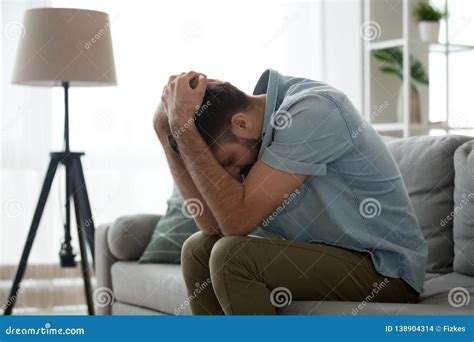Depressed Sad Man Sitting On Couch Holding Head In Hands Stock Photo