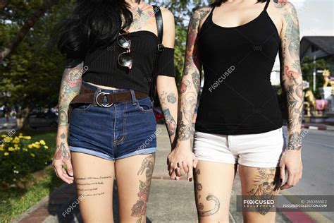 Tattooed Lesbian Couple Holding Hands On The Street In Summer