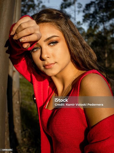 Greeneyed Girl Wearing A Red Blouse Looking Towards The Sun Propped Up On A Tree Trunk In The