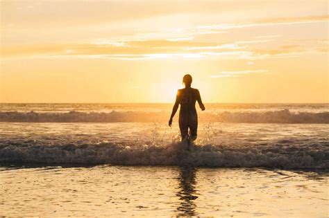 Rear View Of Mid Adult Nude Womans Silhouette Walking Into Ocean At Sunset Stock Photo