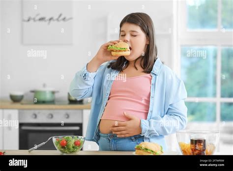 Overweight Girl Eating Unhealthy Burger In Kitchen Stock Photo Alamy