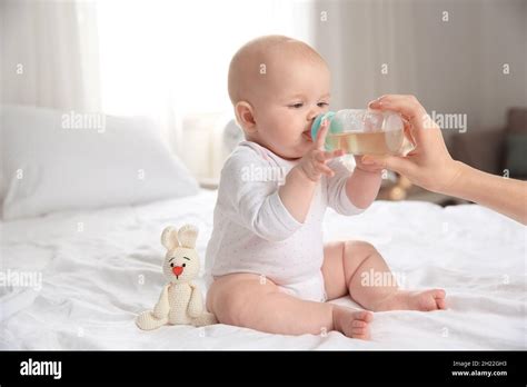 Lovely Mother Giving Her Baby Drink From Bottle On Bed In Room Stock