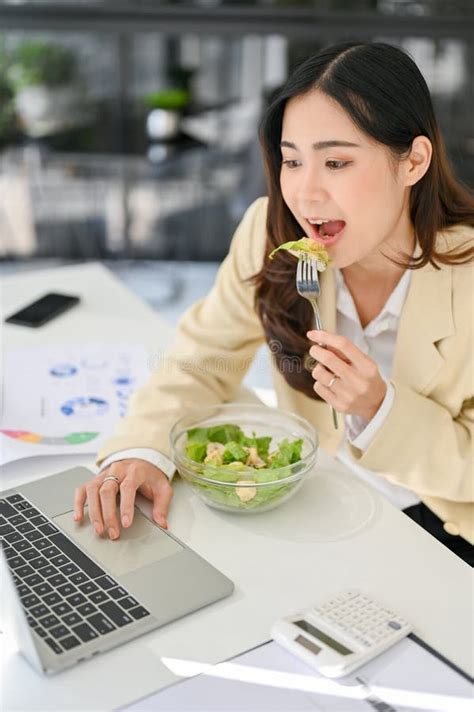 Hungry And Busy Asian Businesswoman Eating Salad Bowl And Working On