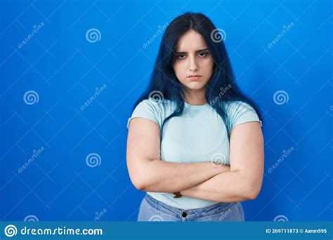 Young Modern Girl With Blue Hair Standing Over Blue Background Skeptic