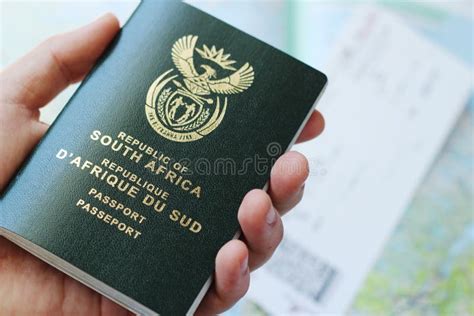 High Angle Shot Of A Person Holding A Passport Over A Plane Ticket And A Geographical Map Stock