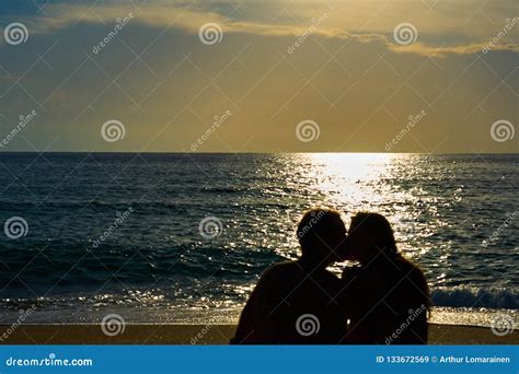 silhouettes of a couple man and woman sitting on a sandy beach and kissing with sunset on the