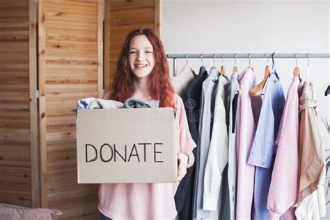 Smiling Young Woman Putting Clothing Into Donation Box Stock Photo