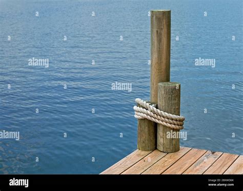 The Corner Of A Boat Dock On A Lake With Rope Wrapped Around Pilings