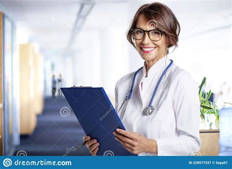 Smiling Female Doctor Standing At Hospital Corridor While Looking At