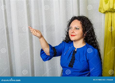 Curly Haired Brunette Woman In Blue Points To Something With Her Hand
