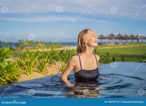 Woman Relaxing In Infinity Swimming Pool Looking At View Stock Photo