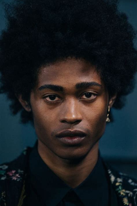 A Young Man With An Afro Wearing A Black Shirt And Flowered Jacket