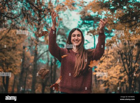 Girl Throwing Leaves In The Air At An Autumn Scenery Forest Smiling At