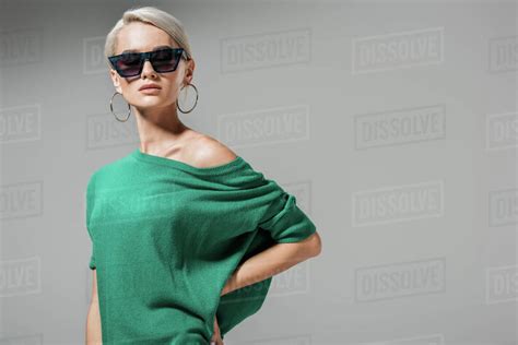 Attractive Female Model In Sunglasses And Green Sweater Posing With Hand On Waist Isolated On