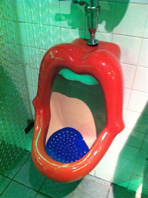 The Urinal Is Shaped Like A Mouth And Has A Blue Ball In Its Mouth