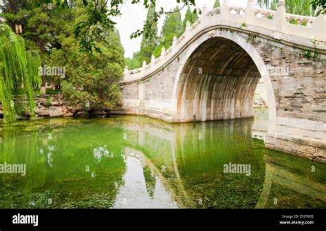 Old Style Stone Chinese Arch Bridge In A Green Garden Pond In Beijing
