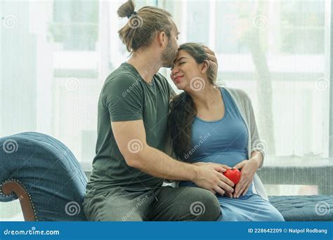 pregnant woman sitting on sofa with husband kissing to pregnant wife relax together in living