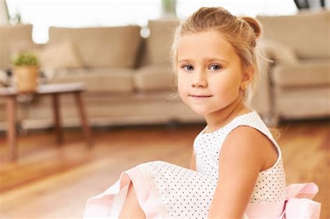 Красивая очаровательная маленькая девочка в праздничном платье с пышной юбкой сидит босиком на
