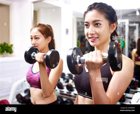 Two Young Asian Women Working Out Exercising In Gym Using Dumbbells