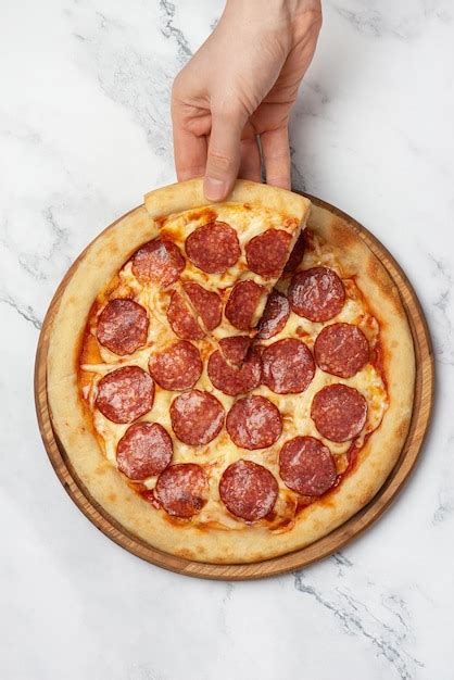 Premium Photo Hand Taking A Slice Of Pepperoni Pizza On A Gray Background