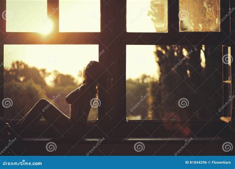 Beautiful Naked Female Sitting On A Window At Sunset Stock Photo