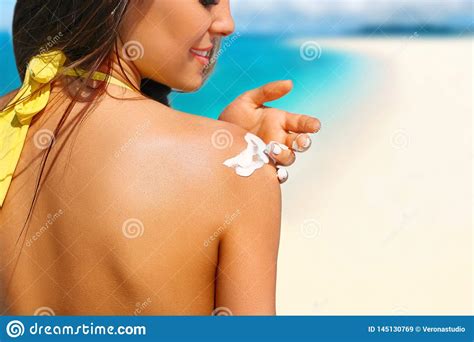 Woman Putting Sunblock Lotion On Shoulder Before Tanning During Summer Holiday On Beach Vacation