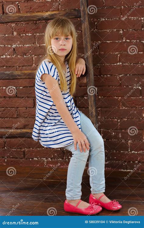 Girl 6 Years Old In Jeans And Vest Sits On A Ladder Near Wall Stock