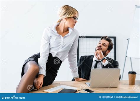 Secretary Sitting On Table While Flirting With Businessman Stock Image