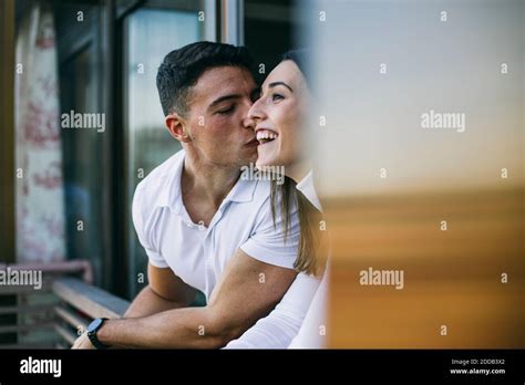 Boyfriend Kissing Woman While Leaning At Balcony Railing Stock Photo