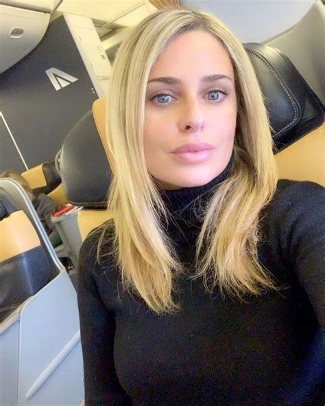 a woman sitting on an airplane seat with her hair in the air and looking at the camera