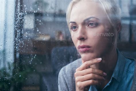 Sad Thoughtful Adult Woman Touching Face At Home Through Window With