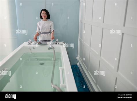 Smiling Assistant Prepares Hydro Massage Bath Full Of Clear Water In