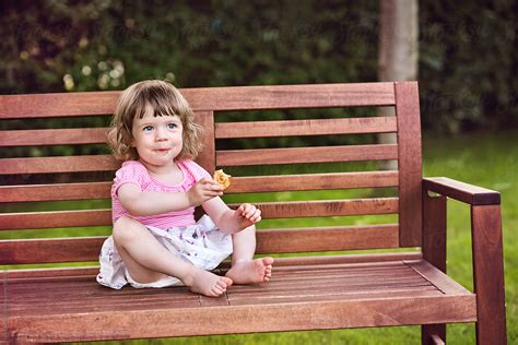 Cutel Little Girl Sitting On A Bench In A Park And Having A Snack By