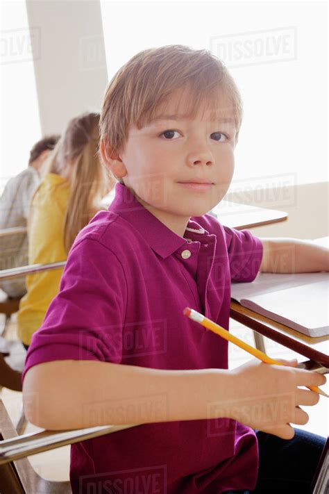 Schoolboy Holding Pencil In Classroom Stock Photo Dissolve