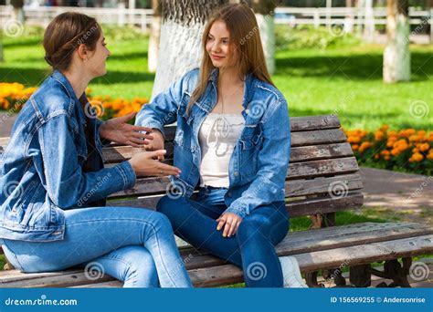 Two Beautiful Girlfriends Are Talking In A Park Sitting On A Bench