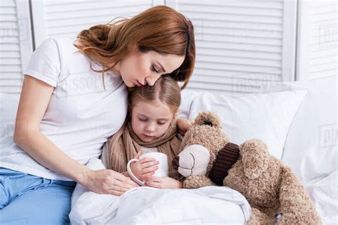 Mother Taking Care Of Sick Daughter And Hugging Her In Bedroom Stock