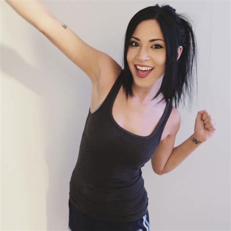A Woman With Black Hair And Piercings Holding Her Arms Up In The Air While Smiling