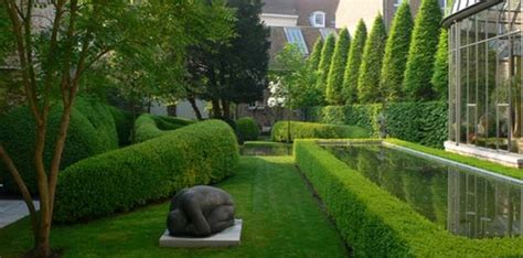 An Outdoor Garden With Hedges Trees And A Sculpture In The Center
