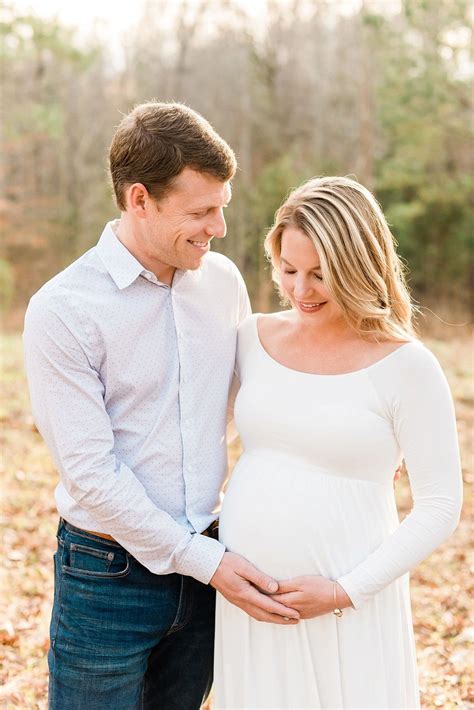 husband and wife together during outdoor maternity session with his hand under her belly while