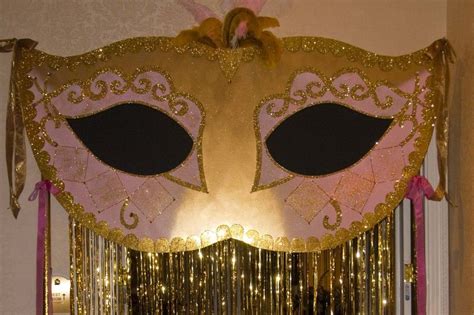 large mask that hangs above entrance to party room with gold foil curtain for guests to walk