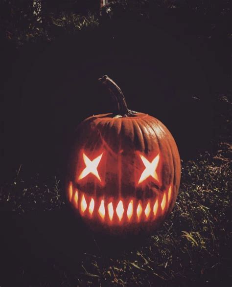 A Carved Pumpkin Sitting In The Grass With Its Eyes Glowing Orange And White Which Are Shaped