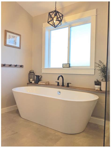 A White Bath Tub Sitting Under A Window Next To A Sink And Shower Faucet