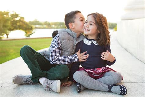 Happy Brother Kissing Sister While Sitting On Retaining Wall Against