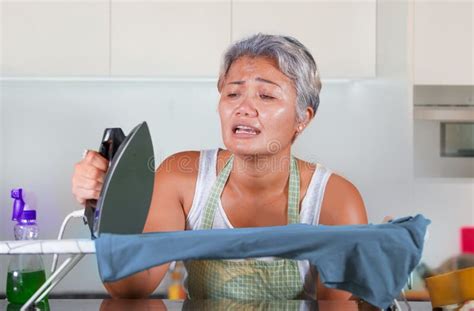 Stressed Middle Aged Asian Woman Ironing In Stress At Home Kitchen Feeling Overwhelmed And Tired