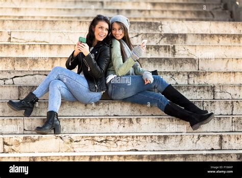 Two Young Women Leaning Against Each Other On Stairs And Holding Cell