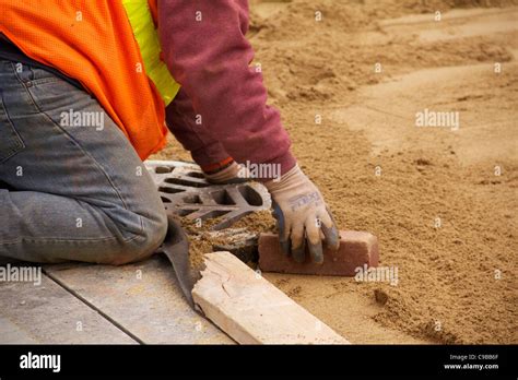 Construction Worker Smooths Sand Paving Bed Around Storm Drain During